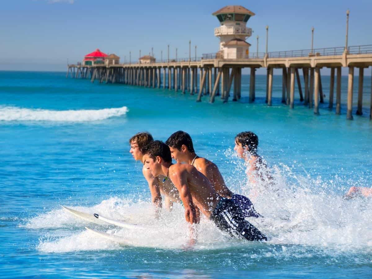 Teenager surfers surfing running jumping on surfboards at Huntinton beach pier California - California Places, Travel, and News.