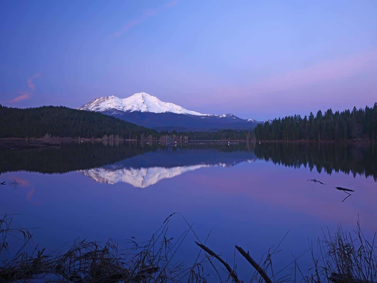 A Reflection Of Mount Shasta Over A Lake During Sunset. - California View