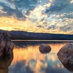 Sunrise and moody clouds on Antelope Lake in Plumas County Northern California USA featuring large boulders and warm reflections. - California Places, Travel, and News.