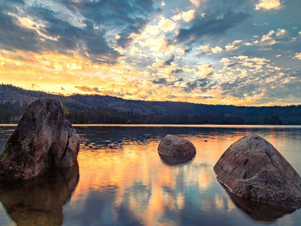 Sunrise and moody clouds on Antelope Lake in Plumas County Northern California USA featuring large boulders and warm reflections. - California Places, Travel, and News.