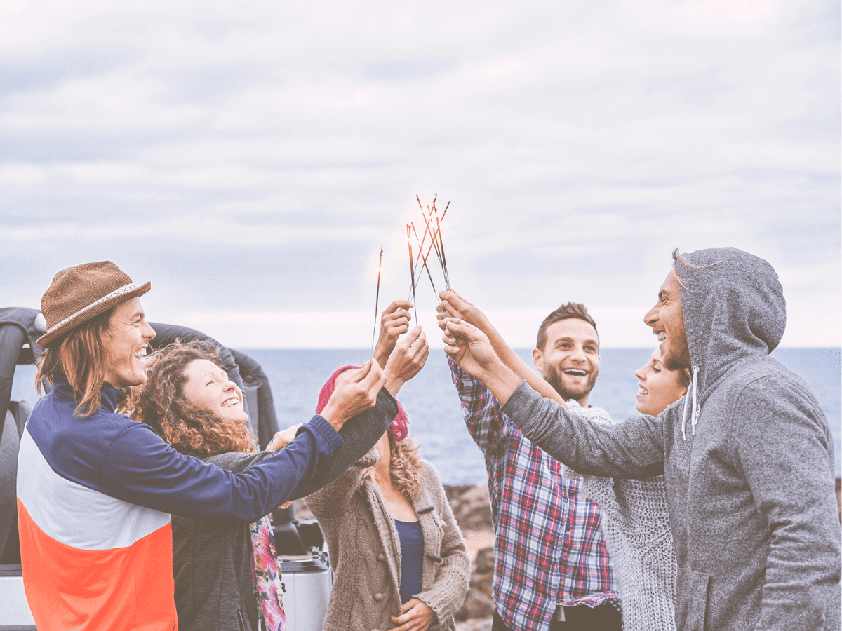 Friends celebrating with sparkling stars fireworks next to ocean - California Places, Travel, and News.