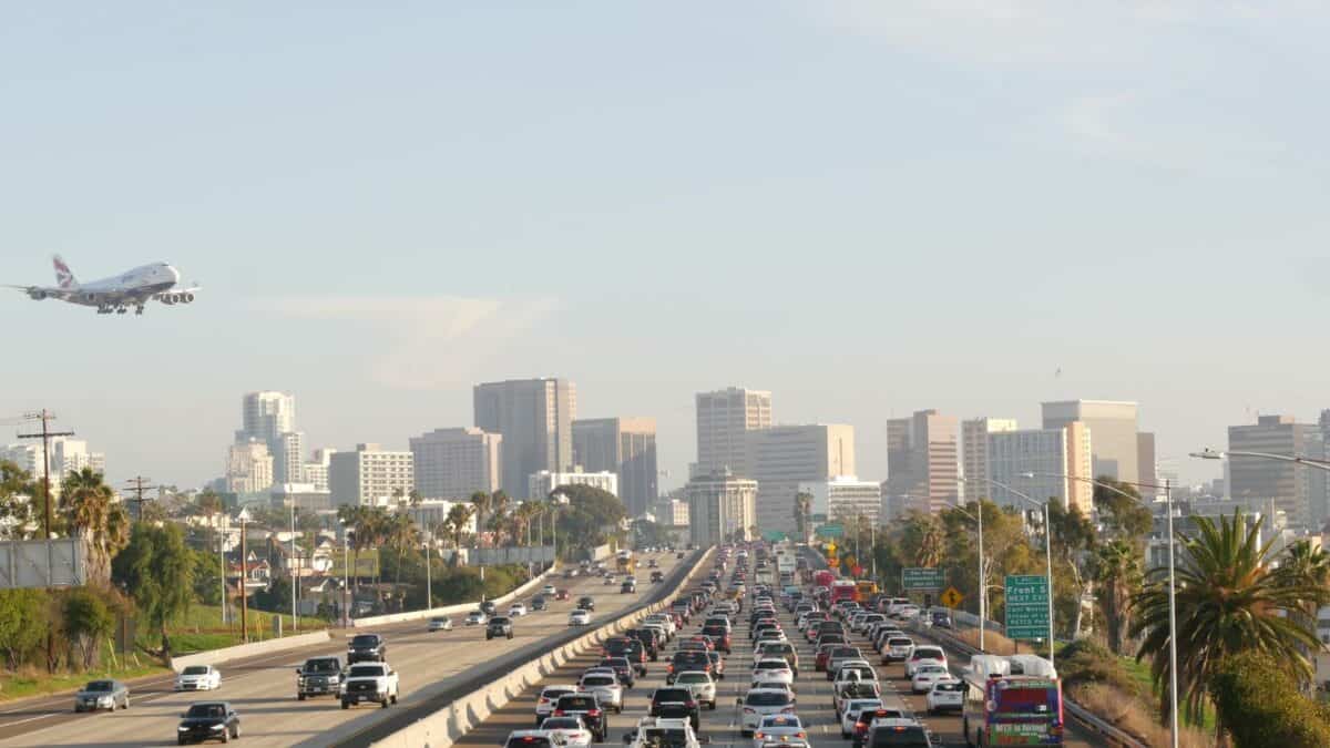 SAN DIEGO CALIFORNIA USA 15 JAN 2020 Busy intercity freeway traffic jam on highway during rush hour. Urban skyline highrise skyscraper and landing plane. Flying airplane - California Places, Travel, and News.