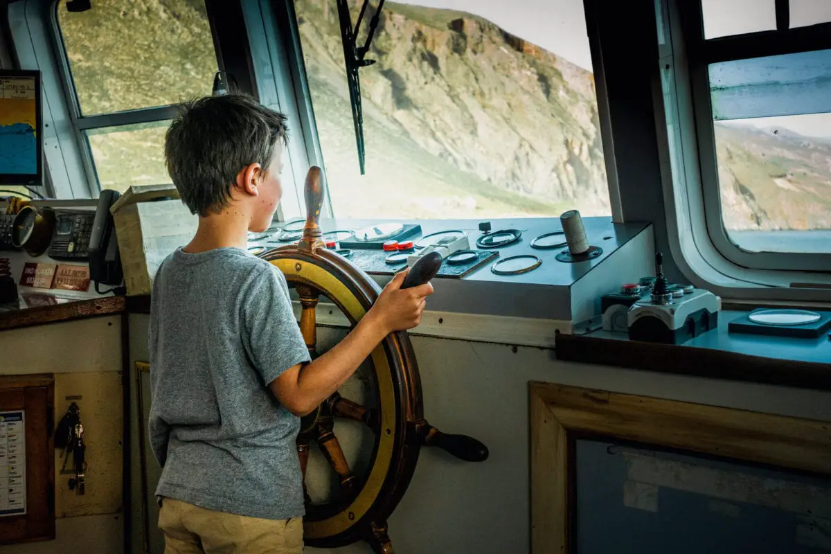 A boy driving a boat firmly holding the helm - California Places, Travel, and News.