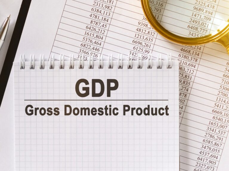 On the table are financial reports a pen a magnifying glass and a notebook with the inscription GDP - California Places, Travel, and News.